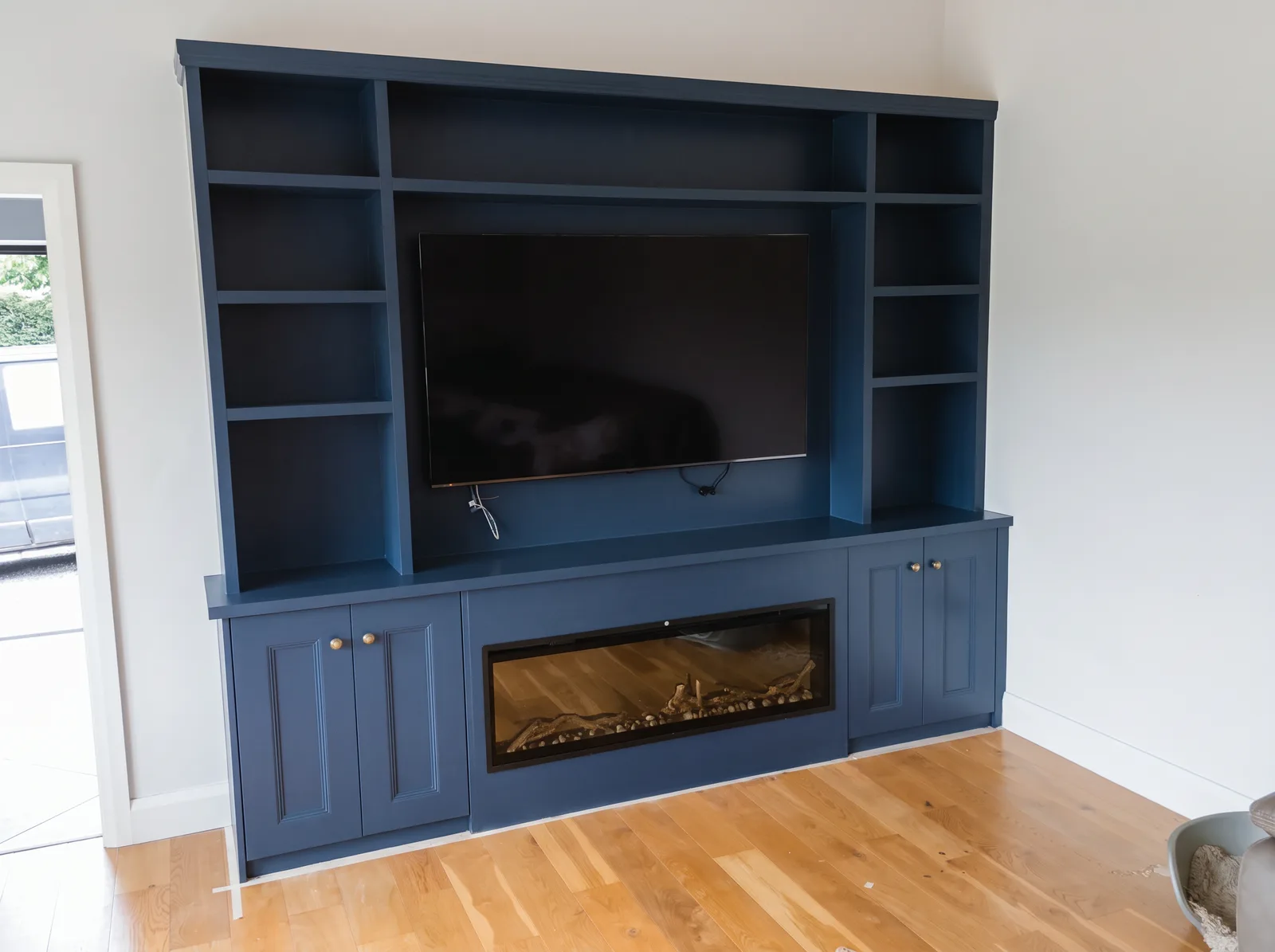 Navy media wall with open display shelving, wall-mounted TV, panelled cupboards and a wide inset fire