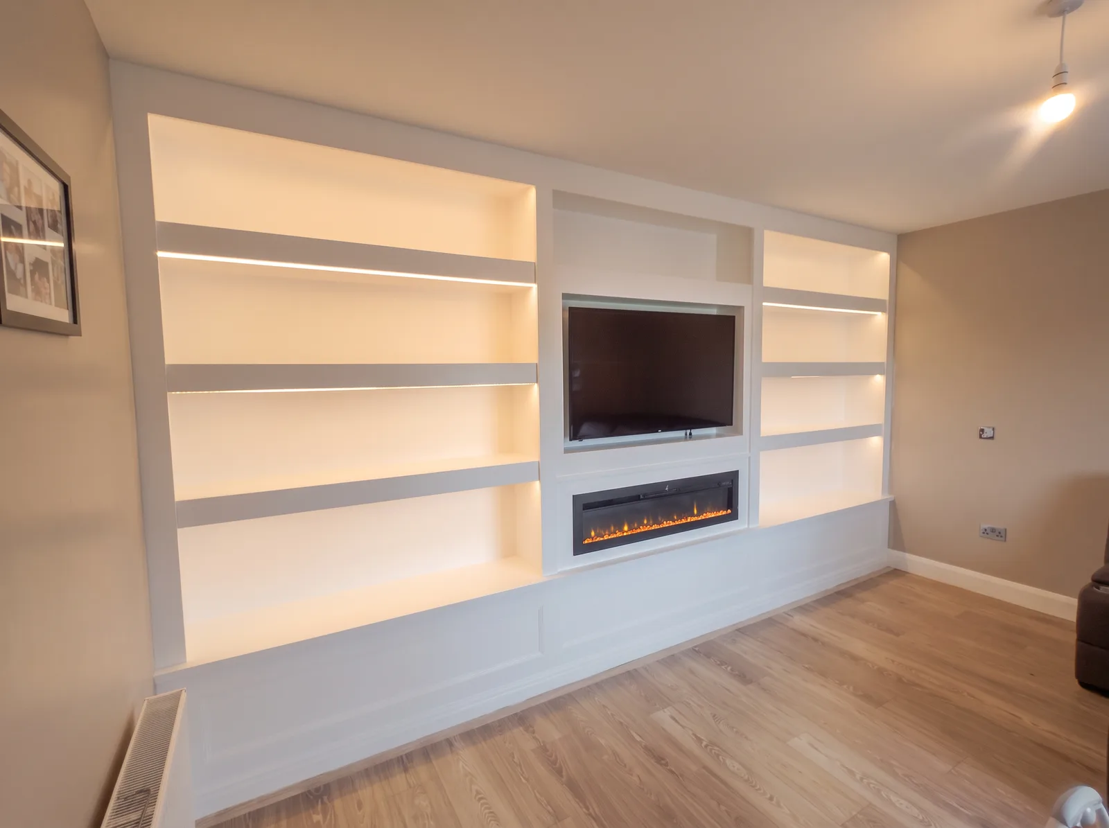 Long white wall of LED-lit floating shelves around a recessed TV and inset fire, on a panelled base
